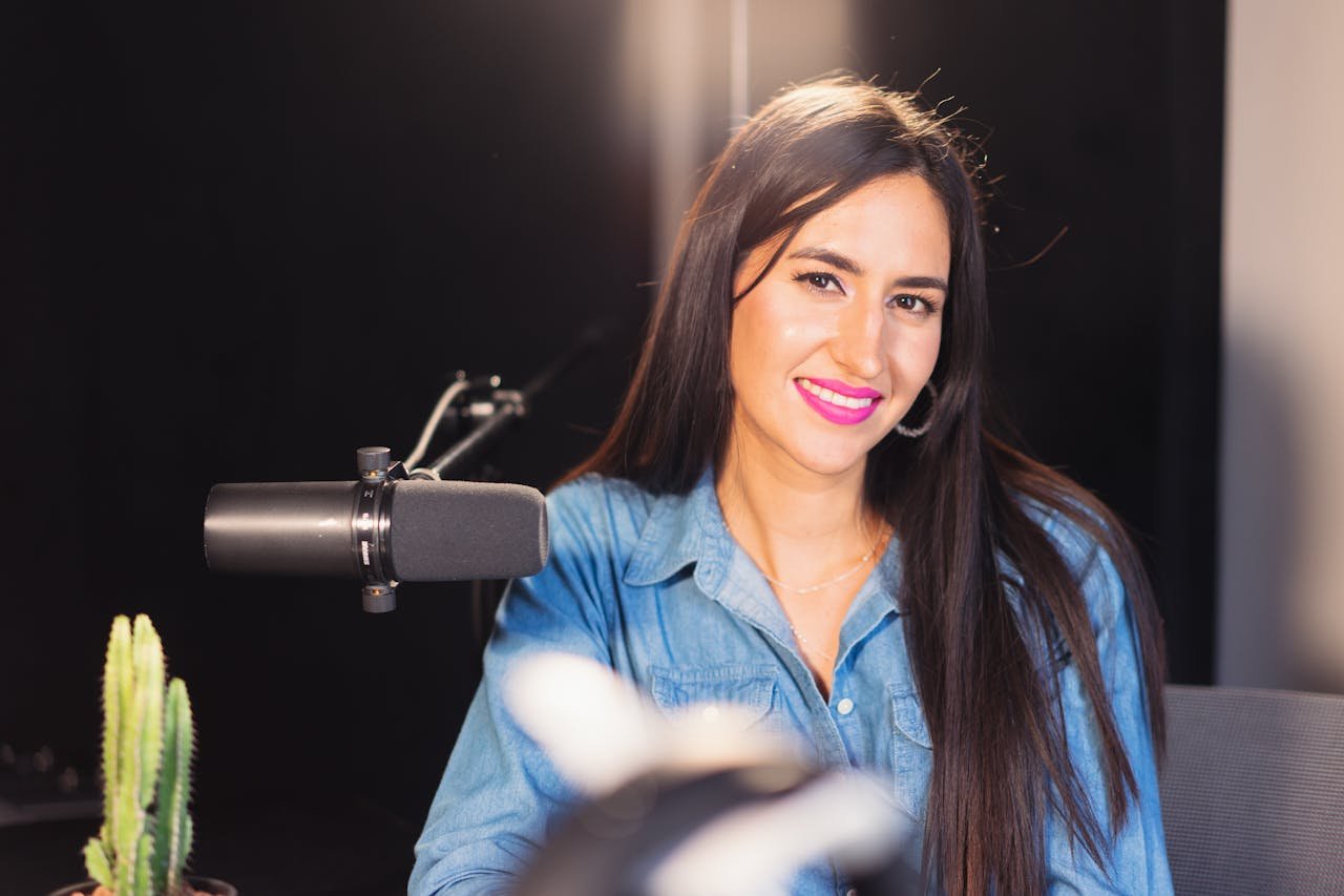 Cheerful woman in denim recording a podcast in a studio with professional equipment.